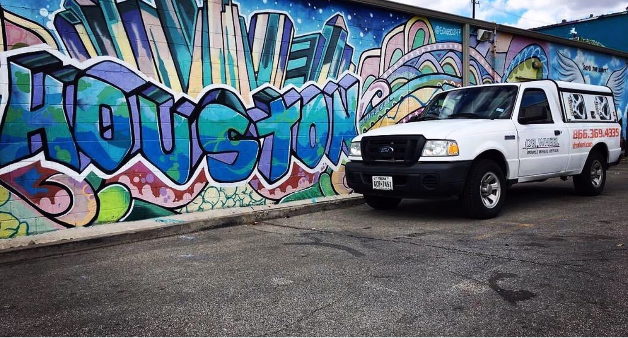 Dr. Wheel service truck parked beside a colorful Houston street mural